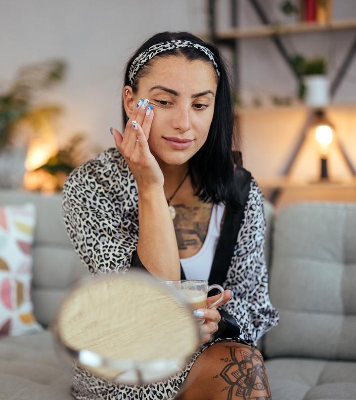 Woman with tattoos applies makeup to her face