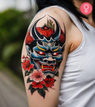A Japanese mask tattoo on a woman’s upper arm A Japanese mask tattoo on a woman’s upper arm