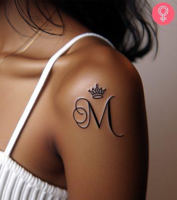 A woman wearing a M letter tattoo with a crown on the upper arm A woman wearing a M letter tattoo with a crown on the upper arm