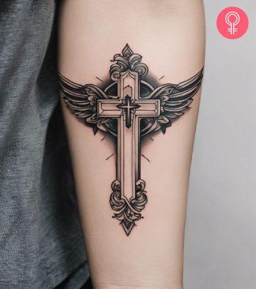 A black and gray cross tattoo with wings inked on the forearm A black and gray cross tattoo with wings inked on the forearm